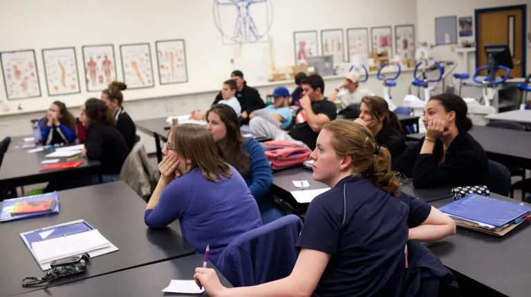 A group of athletic training students in a classroom with skeletomuscular portraits hanging on the wall