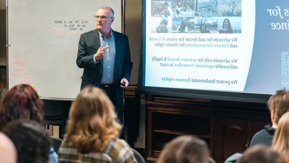 A lecturer standing in front of a presentation speaks to a group of students